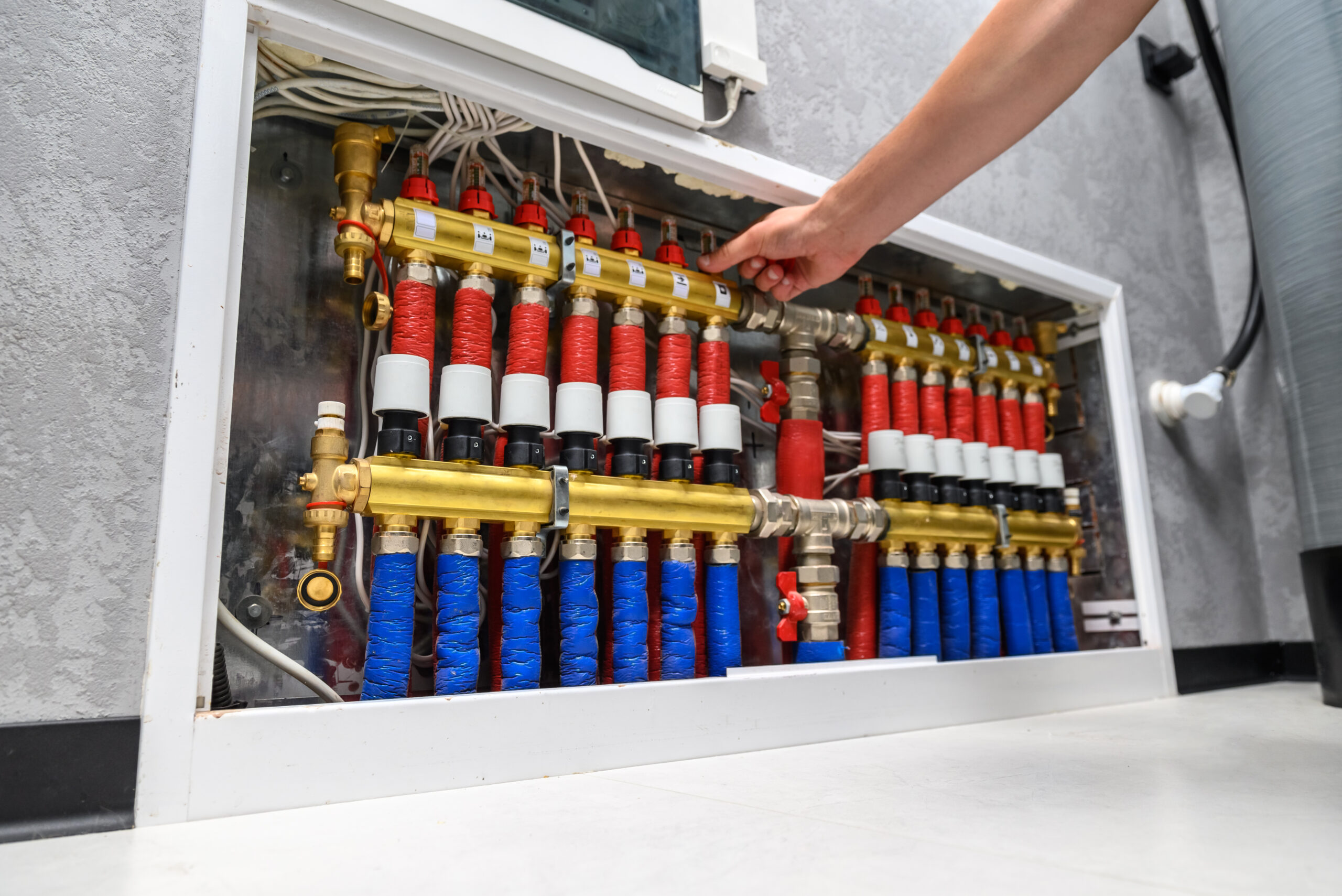 Modern electric boiler in the house. Floor heating manifolds. A man is setting up the system, close-up of a hand