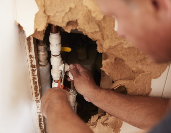 Over shoulder view of middle aged man repairing burst pipe